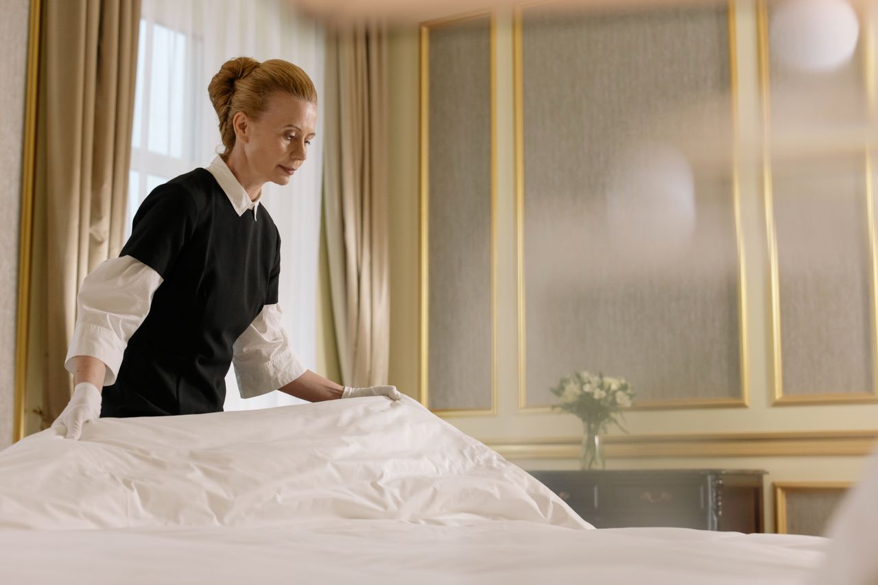 about-01 A professional housekeeper fixes a bed in a luxurious hotel room.